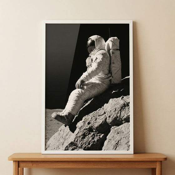 Framed monochrome sitting lunar rock astronaut wall art rests on a wooden console table against a neutral wall.