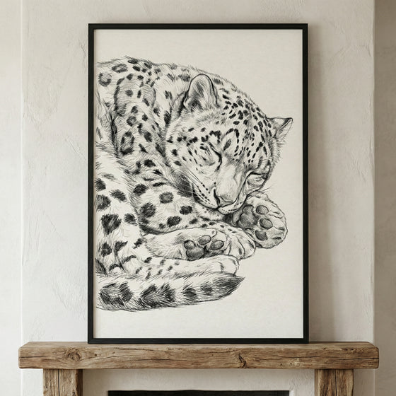 A black and white sketch of a snow leopard curled up and sleeping. The detailed illustration captures the feline's thick, spotted coat and large paws tucked under its head. The artwork is set in a simple black frame and rests on a rustic wooden mantelpiece against a light-colored, textured wall.