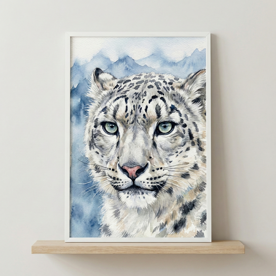 A vertical watercolor illustration of a snow leopard's face is shown in a white frame. The leopard has dense, off-white fur covered in dark grey and black spots, with large, pale-green eyes and long white whiskers. Behind the animal, soft blue mountains are visible in a misty style. The framed piece rests on a light-toned wooden shelf against a plain, off-white wall.