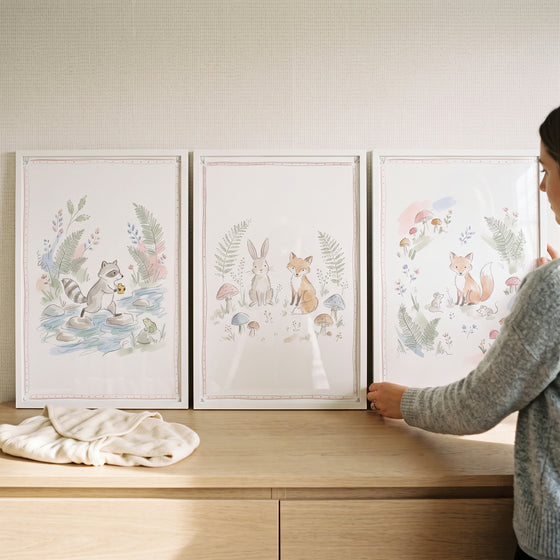 A woman displays a soft botanical forest animals wall art set of 3 featuring a raccoon, rabbit, and foxes in watercolor.