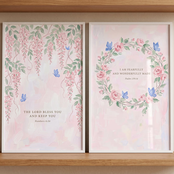Soft floral bible verse wall art set of 2 with pink flowers and blue butterflies in white frames on a wooden shelf.
