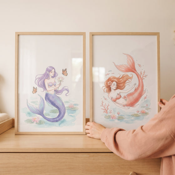 Soft pastel botanical mermaid wall art set of 2 in light wood frames being adjusted on a wooden dresser.