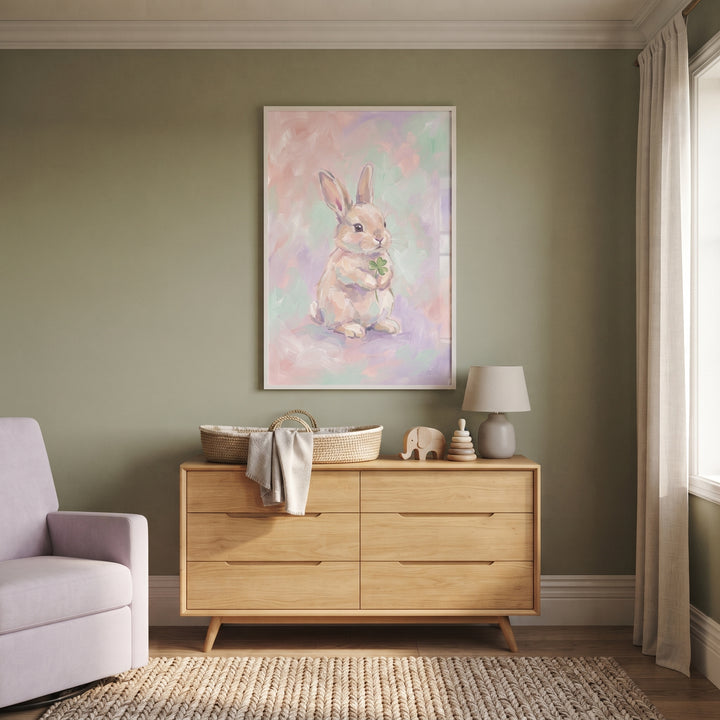Soft pastel clover bunny wall art hangs above a wooden dresser in a sage green room with a moses basket and purple chair.