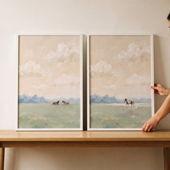 Soft peach sky horses wall art set of 2 displays horses in a field under a cloudy sky in matching white frames.