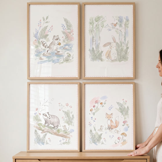 Soft pencil forest animals wall art set of 4 featuring a raccoon, rabbit, badger, and fox in light wood frames on a wall.