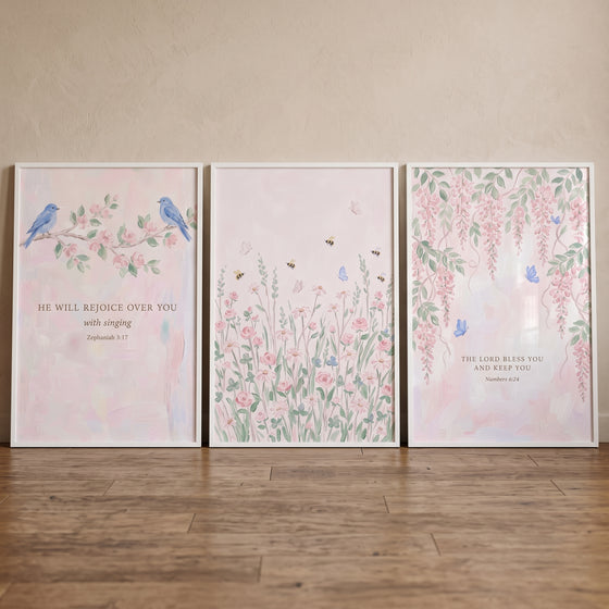 Framed soft pink watercolor garden wall art set of 3 with blue birds, flowers, and scripture on a wood floor.
