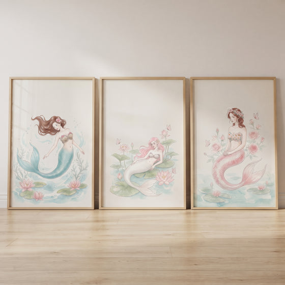 Soft watercolor butterfly mermaid wall art set of 3 in wooden frames leans against a wall on a light wood floor.