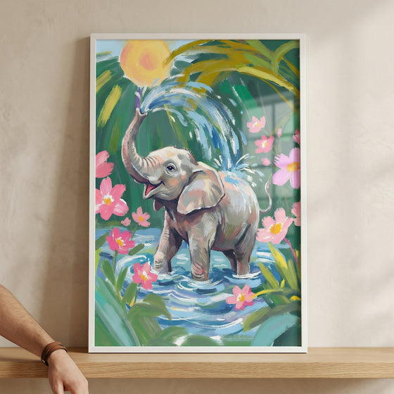 A framed, vibrant illustration features a cheerful young elephant standing in shallow blue water. The elephant has its trunk raised, spraying a fountain of water into the air. Around the elephant are bright pink flowers and lush green tropical foliage. A large, glowing yellow sun shines from behind the leaves.