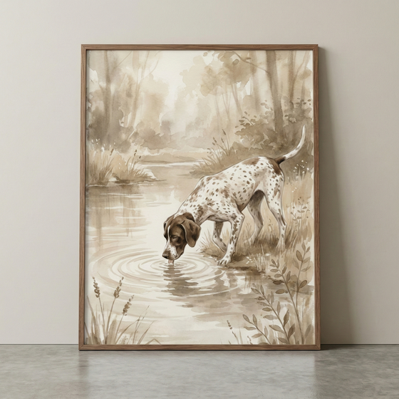 A sepia-toned watercolor illustration of a spotted dog, reminiscent of a hunting breed, leaning over to drink from a pond. Soft ripples emanate from its muzzle where it touches the water's surface. The scene is set in a peaceful natural environment with tall reeds in the foreground and a hazy forest in the background. The monochromatic brown palette creates a warm, vintage aesthetic. The artwork is presented in a simple wooden frame, resting against a neutral-colored wall.