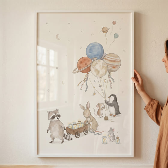 Hand holds framed star jar wagon animals wall art featuring a raccoon, bunny, and penguin holding planet balloons.