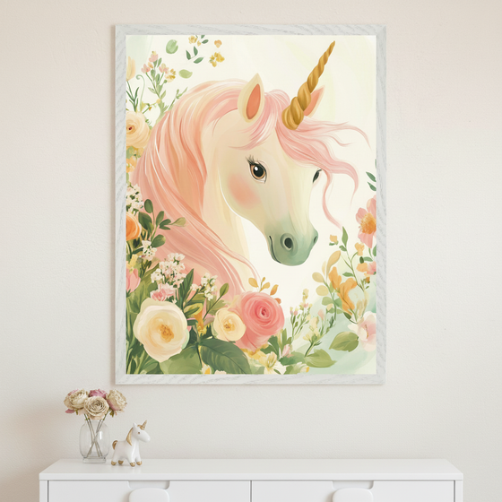 A person in a beige sweater holds up a framed illustration of a unicorn with a golden horn, soft pink mane, and gentle expression, surrounded by pastel-colored flowers including roses and greenery. The whimsical artwork has a dreamy, fairytale-like style, and the person’s face is hidden behind the frame.