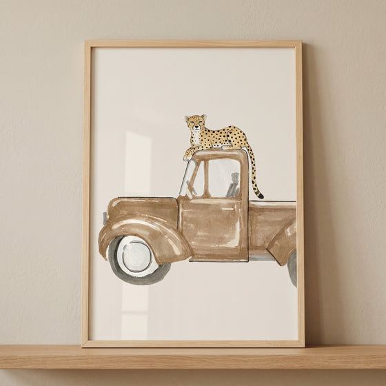 Framed vintage brown truck cheetah wall art showing a spotted cheetah resting on the roof of a classic pickup truck.