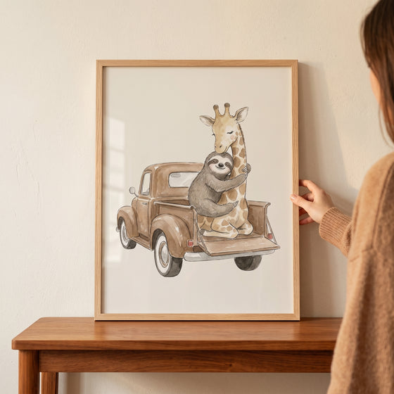 Framed vintage truck sloth giraffe wall art showing a sloth hugging a giraffe in a pickup, held by a person.