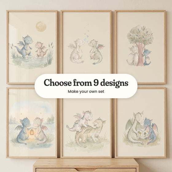 Six baby dragon prints in light wood frames in two rows above a light wood cabinet on a cream wall: two dragons splashing in a puddle, two dragons face to face with floating hearts, two dragons peeking round a tree, two dragons holding a glowing lantern, a little dragon riding on a bigger one's back and two dragons reading a book, with a label reading Choose from 9 designs, Make your own set