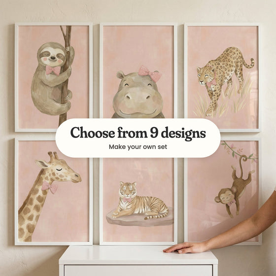 Six safari animal prints in white frames standing on a white dresser, with a woman's hand resting beside them: a sloth hugging a branch, a hippo with a pink bow, a leopard in tall grass, a giraffe in a bow tie, a tiger resting on a rock and a monkey swinging from a vine, with a label reading Choose from 9 designs, Make your own set