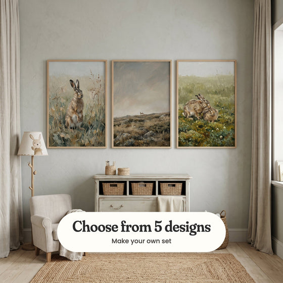 Pale grey nursery with three hare prints in light wood frames above a cream dresser with woven baskets, beside a bunny lamp, a small cream armchair and a jute rug: Wild Meadow Hare, Wild Moorland Runner and Wild Hare Affection, with a label reading Choose from 5 designs, Make your own set