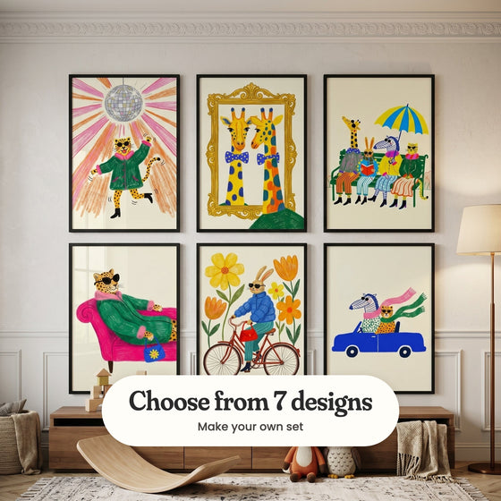 Cream panelled kids' room with six animal prints in black frames in two rows above a low wood sideboard with wooden blocks, a wooden balance board, plush toys and a knit throw, beside a floor lamp and a basket: Disco Leopard Groove, Dapper Giraffe Reflection, Stylish Safari Social, Chic Leopard Lounge, Stylish Bunny Ride and Wild Road Trip, with a label reading Choose from 7 designs, Make your own set