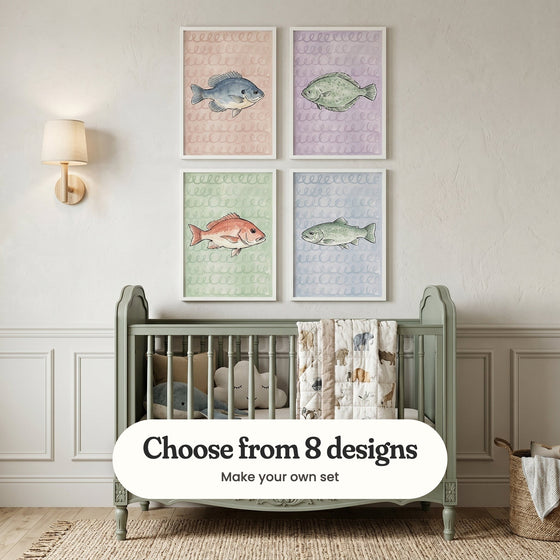 Cream nursery with four fish prints in white frames in two rows above a sage green crib with a quilt and plush toys, beside a wall light and a woven basket: Azure Sunfish Sketch, Lavender Sea Flounder, Red Snapper Swirls and Speckled Stream Trout, with a label reading Choose from 8 designs, Make your own set