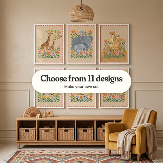 Six folk-art style safari animal prints in white frames, each with a pink border edged in red dashes, above a low wooden cubby shelf with woven baskets and wooden toys, beside a mustard armchair: a giraffe and calf reaching for a branch, an elephant and calf, and a cheetah with two cubs, all among bright flowers, with a label reading Choose from 11 designs, Make your own set