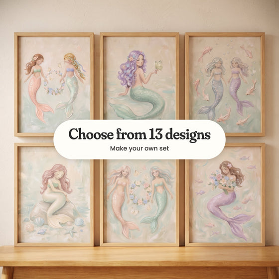 Six mermaid prints in light wood frames in two rows leaning on a wood bench: two mermaids holding a flower wreath, a lavender-haired mermaid with a butterfly on her hand, two mermaids among pink fish, a rose-haired mermaid sitting on a rock, a peach-tailed and a mint-tailed mermaid by a wreath, and a mermaid hugging a bouquet, with a label reading Choose from 13 designs, Make your own set