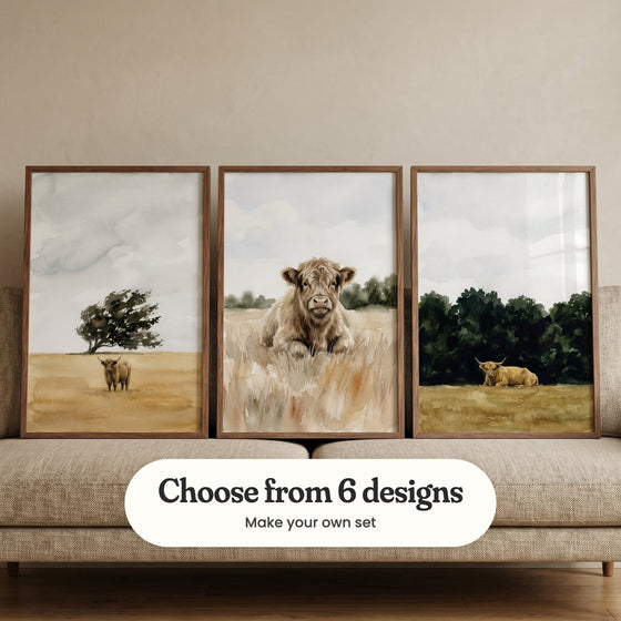 Three highland cow prints in walnut frames leaning on a beige linen sofa: a cow standing in a golden field under a windswept tree, a shaggy calf in tall grass and a golden cow lying in front of dark green trees, with a label reading Choose from 6 designs, Make your own set