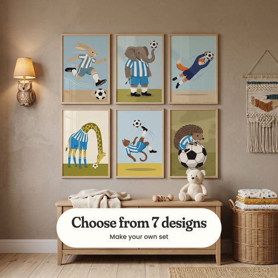 Taupe kids' room with six soccer animal prints in light wood frames in two rows above a light wood bench with a teddy bear, a knit throw and wooden toys, beside an owl wall lamp, a woven wall hanging and a wicker basket of folded blankets: Speedy Bunny Kick, Elephant Soccer Star, Clever Goalie Fox, Spotted Soccer Star, Midair Soccer Cat and Sporty Spiky Friend, with a label reading Choose from 7 designs, Make your own set