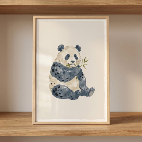 Framed watercolor bamboo eating panda wall art rests on a light wooden shelf in a neutral room.