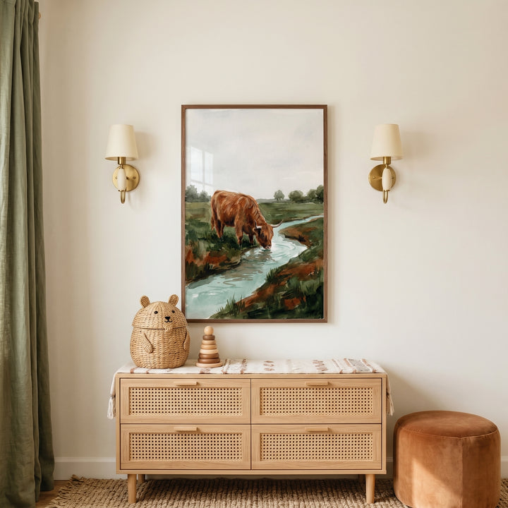 Watercolor drinking highland cow wall art between wall lamps above a rattan dresser with a bear basket and stacking toy.
