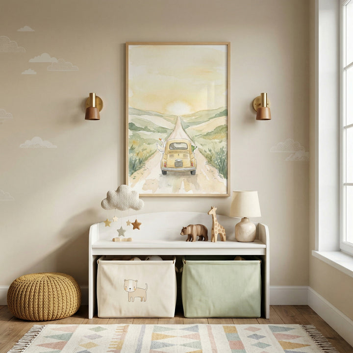 A cozy, neutral-toned nursery or playroom features a central piece of framed wall art depicting a soft, watercolor-style landscape. In the illustration, a vintage-style yellow car travels along a winding dirt path through green hills, heading toward a glowing sun on the horizon. The wall is a warm beige, accented with delicate white cloud decals and flanked by two modern gold and brown wall sconces.