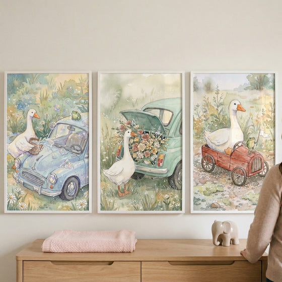This set of three framed wall art pieces features a whimsical series of watercolor illustrations depicting white geese and vintage-style vehicles. The scenes are rendered in soft, pastel tones, creating a gentle and charming atmosphere suitable for a nursery or child's room.