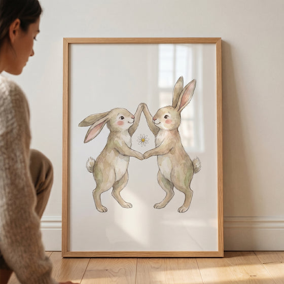 Watercolor high five rabbit wall art in a wooden frame shows two brown bunnies touching paws over a small daisy.
