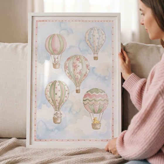 Framed watercolor hot air balloon wall art featuring pastel balloons and small animals in a soft blue sky.
