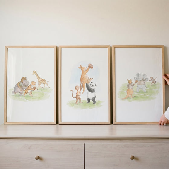 Watercolor rugby safari animals wall art set of 3 in light wood frames resting on a light-colored dresser.