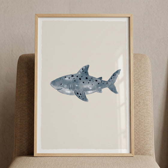 Watercolor spotted shark wall art in a light wood frame, resting on a beige chair against a neutral background.