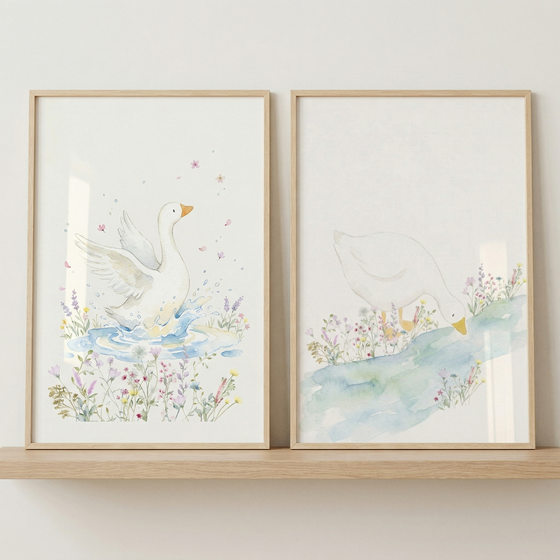 Two framed illustrations in a soft watercolor style sit side-by-side on a light wood shelf. The image on the left features a white goose with its wings spread, splashing in a small blue pond surrounded by delicate wildflowers. The image on the right shows a white goose leaning down toward a flowing blue stream, also amidst a variety of colorful flowers. Both artworks use a pastel color palette and are encased in thin, light-colored wooden frames against a plain, off-white wall.