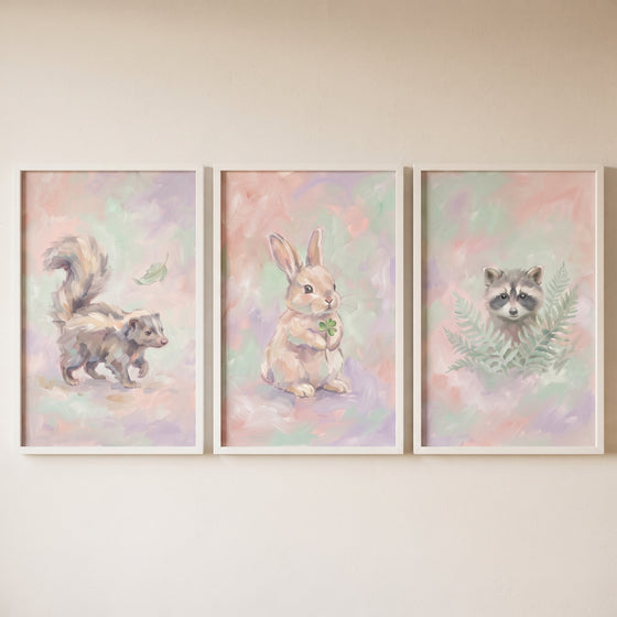 Whimsical pastel woodland animal wall art set of 3 with a skunk, rabbit with clover, and raccoon in white frames.