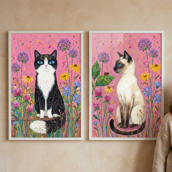 Two framed vertical illustrations of cats are displayed side-by-side. On the left, a black and white tuxedo cat with starry-textured fur and bright blue eyes faces forward in a garden of purple, yellow, and blue flowers against a pink sky. On the right, a light-colored cat with dark brown markings and blue eyes sits in profile among similar flora. The whimsical style features rich textures and a vibrant color palette, both set within simple white frames.