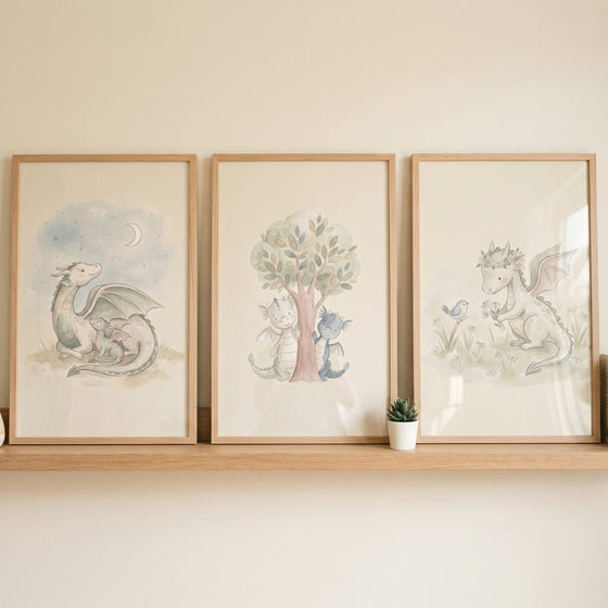 Whimsical watercolor baby dragon wall art set of 3 in wood frames featuring a moon, tree, and flower crown on a shelf.