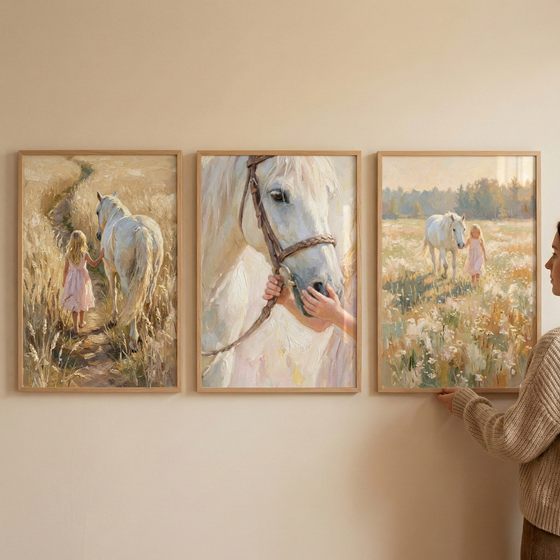 A photograph shows three vertical wooden-framed art pieces hung on a beige wall. The artwork depicts scenes in a soft, textured style with visible brushstrokes. In the left frame, a young girl in a light pink dress and a white horse are seen from behind, walking down a path through fields of tall, golden grass. The middle frame features a close-up of the horse's face, with a child's hands gently touching its muzzle.