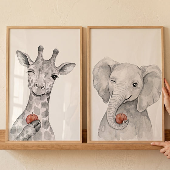 Framed giraffe and elephant illustrations in a winking red apple animals wall art set of 2 on a wooden shelf.