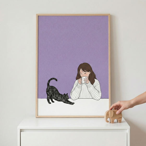 A light wood-framed illustration sits on a white dresser against a plain wall. The artwork depicts a woman with long brown hair in a white ribbed sweater holding a white mug to her face. Beside her, a black cat is shown stretching on a white surface against a light purple background. To the right of the frame, a person's hand reaches for a small, minimalist wooden elephant figurine.