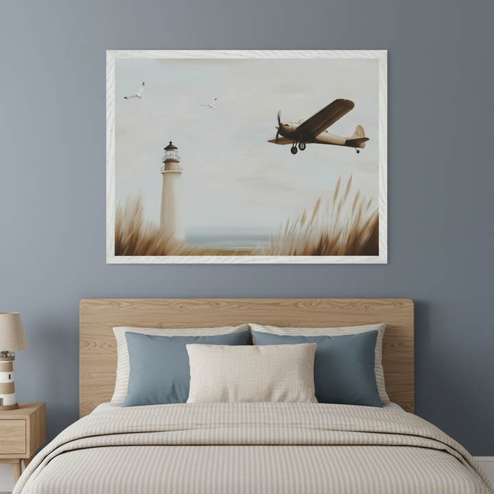 Modern bedroom with a wooden bed frame and headboard. A large framed painting hangs centered above the bed, depicting a lighthouse by the ocean with tall grasses, a vintage airplane flying, and two seagulls. A wooden nightstand with a lighthouse lamp is to the left of the bed.