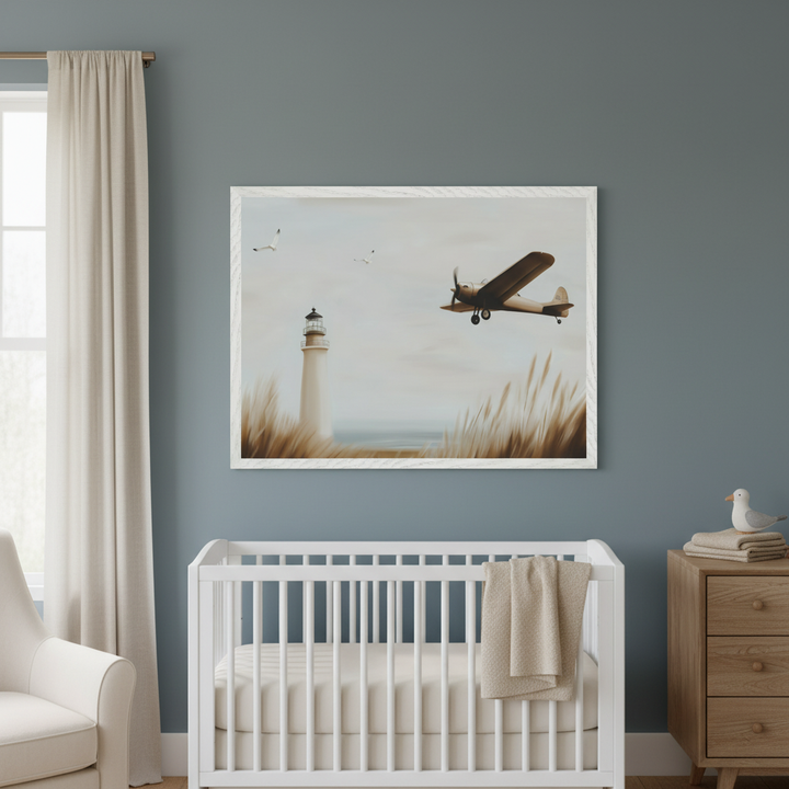 Modern nursery with a white crib, wood dresser, and armchair. A large white-framed print of a lighthouse, a plane, and seagulls over a grassy coast hangs centered above the crib on a blue wall.