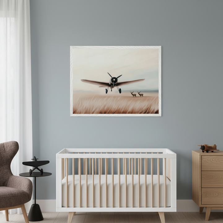 Modern nursery with a white and wood crib against a gray wall. A large framed painting of a vintage airplane taking off over golden grass with two deer hangs centered above the crib. A wooden dresser is on the right, and a brown armchair with a black side table is on the left.