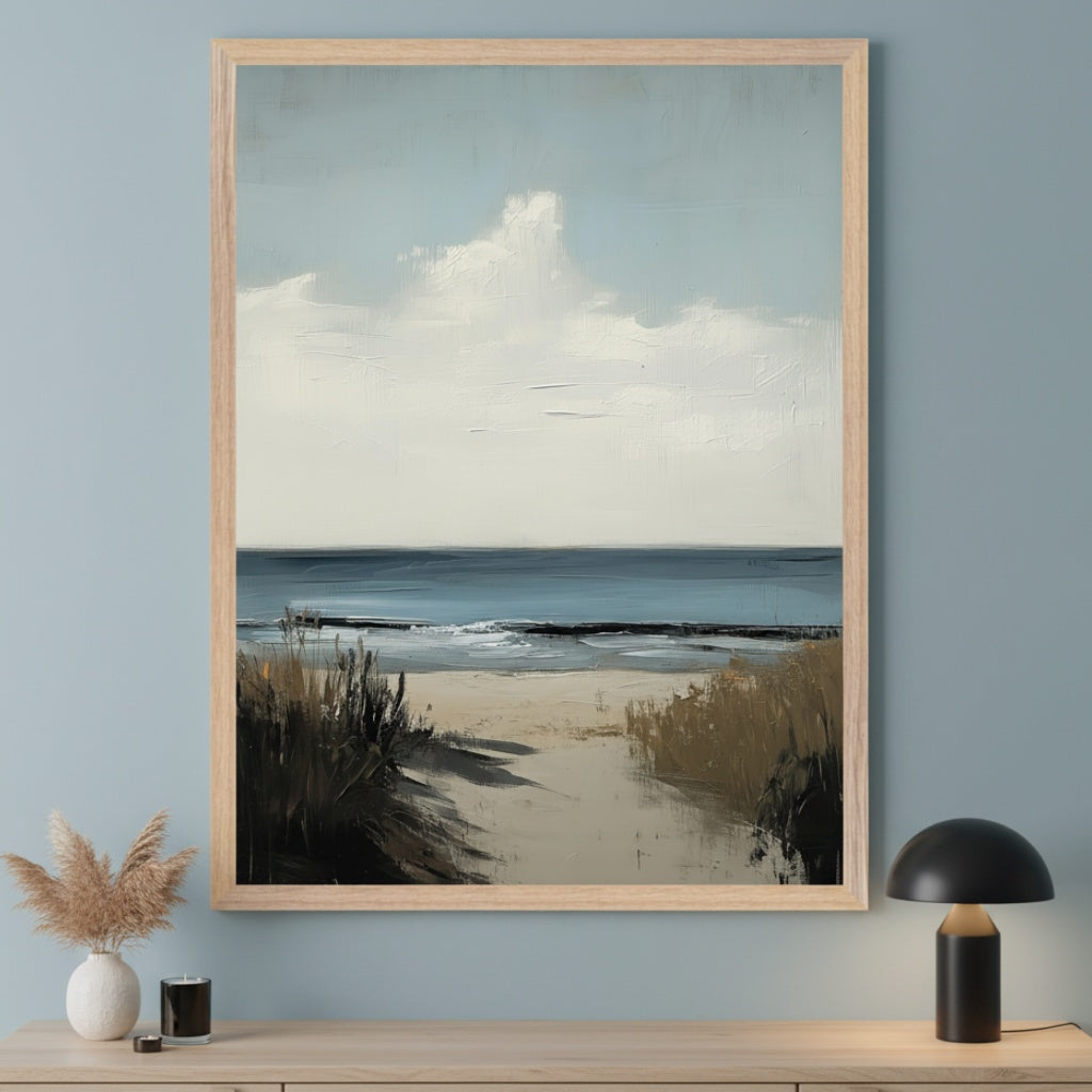 Modern room with a light wooden console table. A large, light-framed abstract beach landscape painting hangs centered above the table, showing a path through dunes to the sea under a cloudy sky.