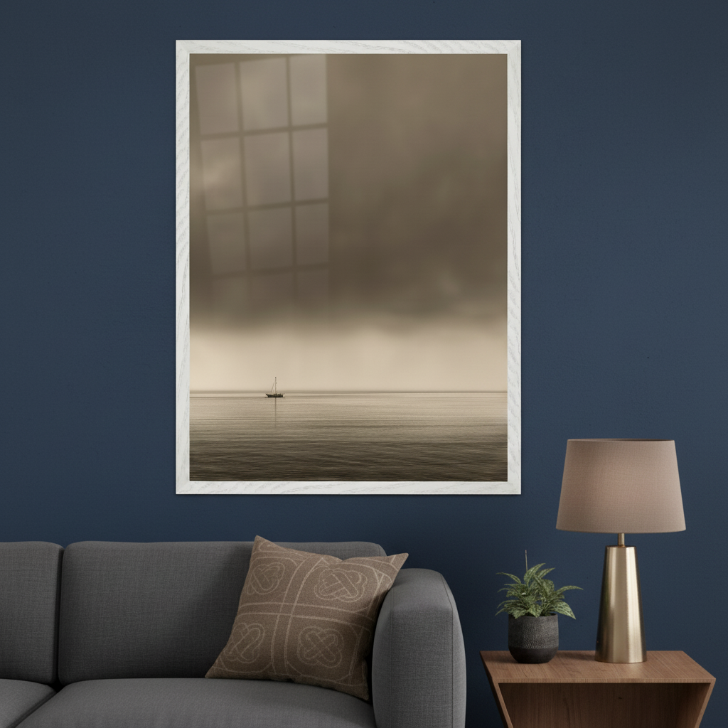 Living room with a gray sofa and a wooden side table holding a lamp. Centered above the sofa, a large white-framed sepia-toned artwork depicts a small sailboat on calm water under a cloudy sky.