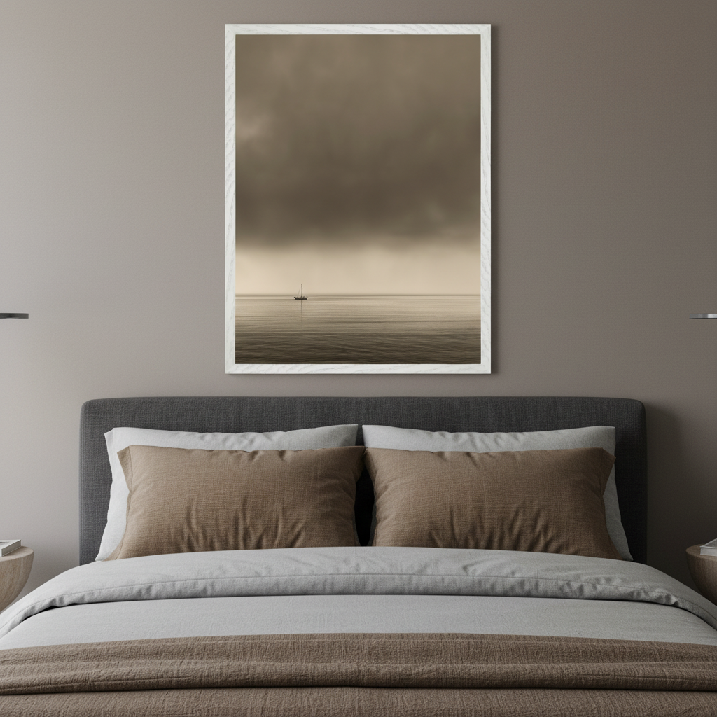 Modern bedroom with a bed featuring a gray headboard. A large framed print of a sepia-toned sailboat on calm water under a cloudy sky hangs centered above the bed.