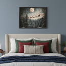 Bedroom with a beige upholstered bed and colorful pillows. A framed Christmas painting hangs above the bed, depicting Santa and reindeer flying a sleigh over a snowy pine forest under a full moon and starry night sky.