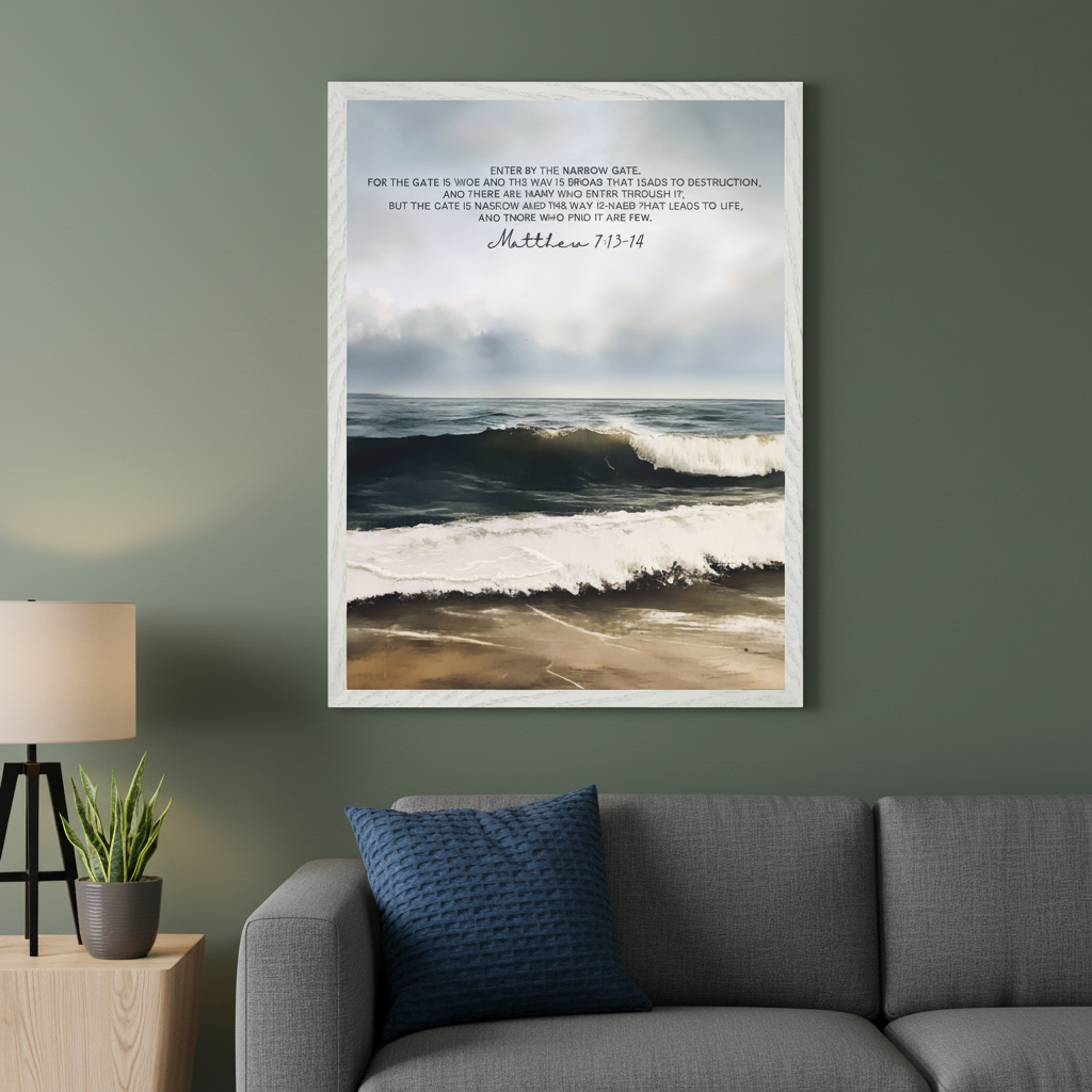 Modern living room with a gray fabric sofa, light wood side table, lamp, and plant. A large framed print of an artistic beach scene with crashing waves under a cloudy sky and overlaid Bible verse Matthew 7:13-14 hangs above the right side of the sofa on a green wall.