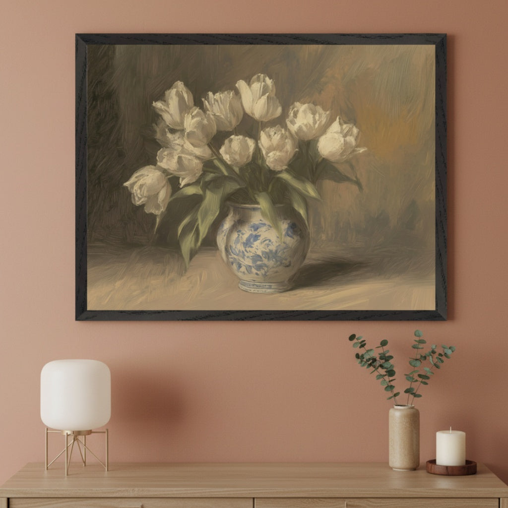 Modern room with a wooden dresser. A black-framed painting of white tulips in a blue vase hangs centered above the dresser. A white lamp, a small vase with green sprigs, and a candle are on the dresser.